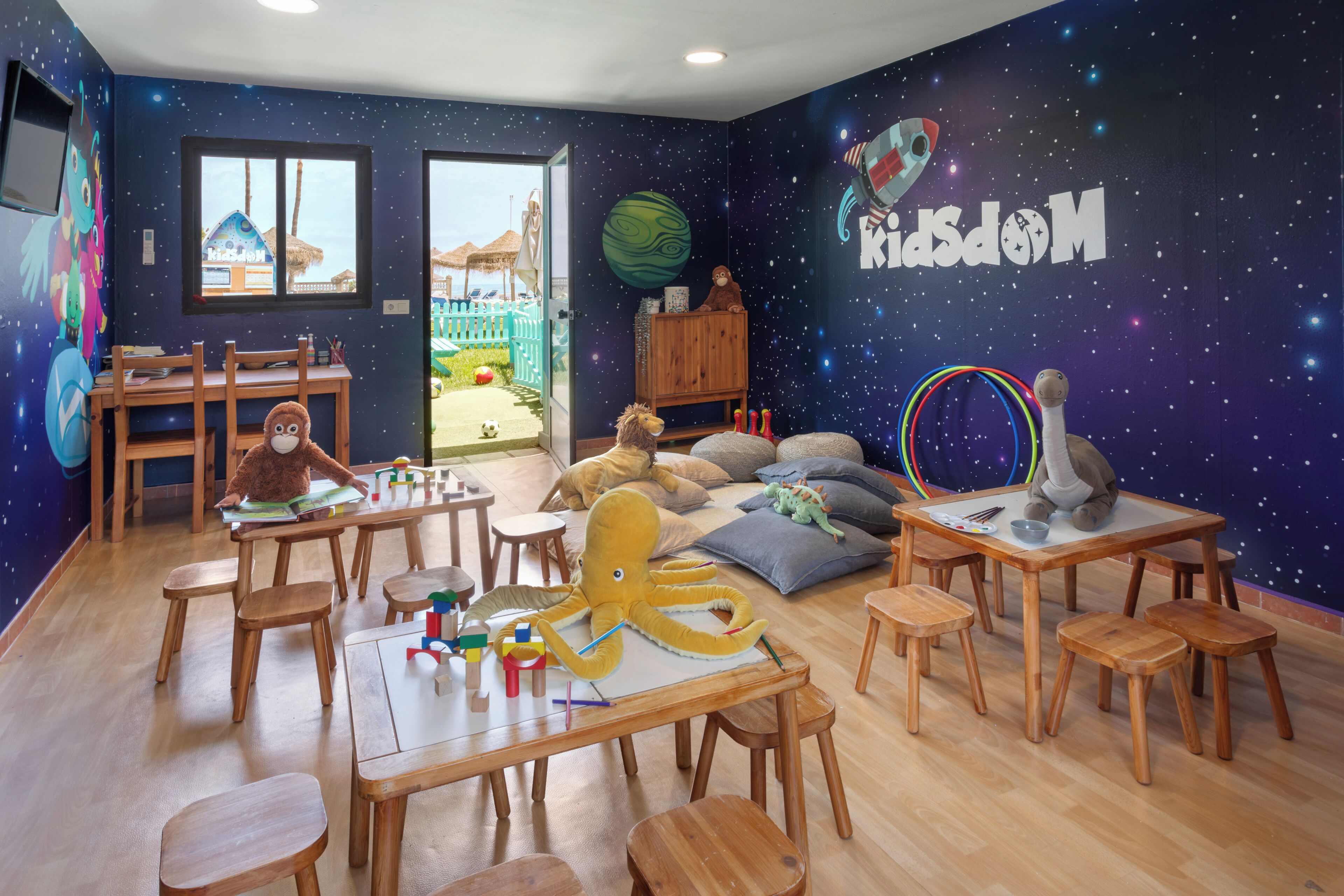 Un cuarto de juegos infantil con un mural de estrellas en la pared, muebles de madera y diversos juguetes.