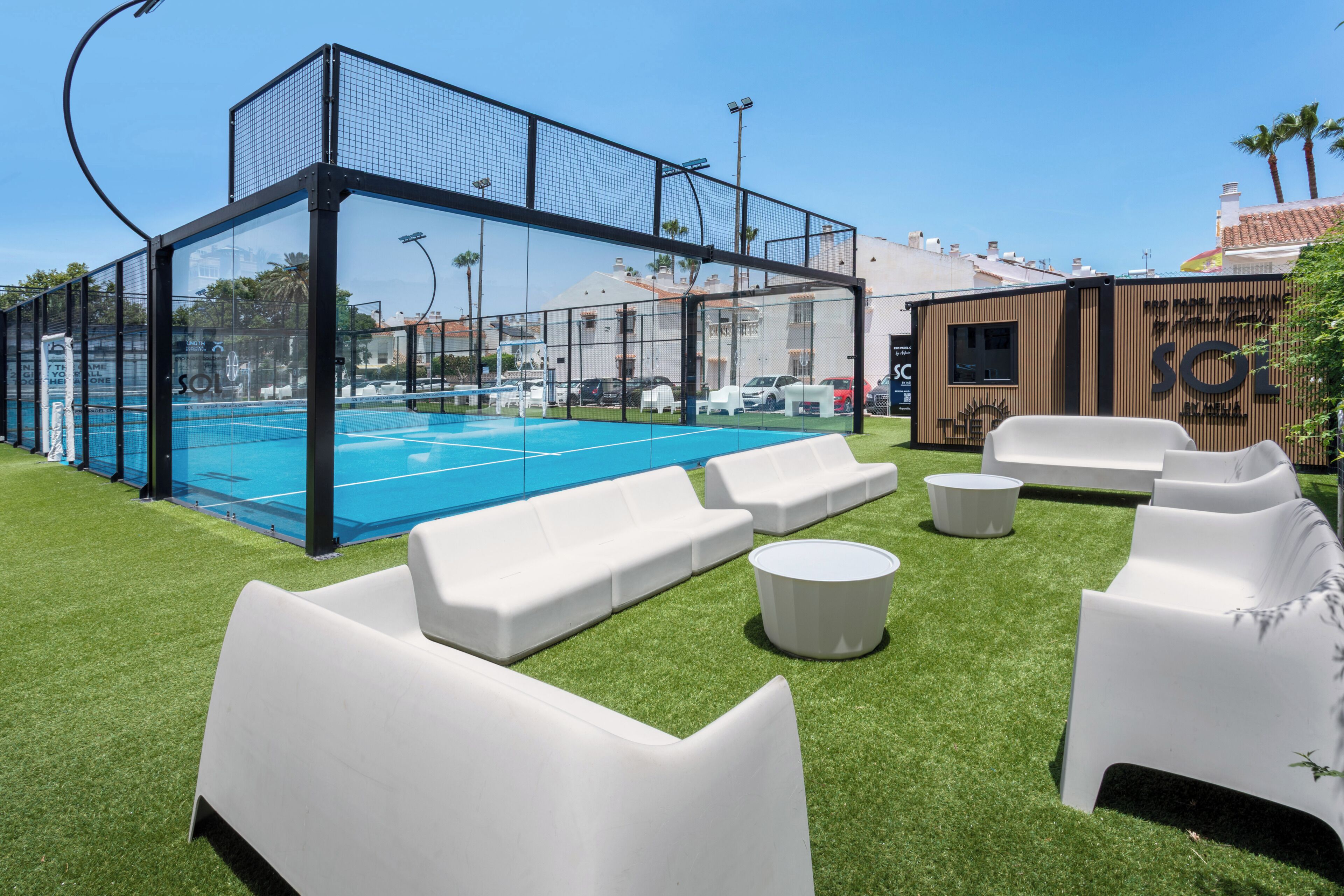 A pool area with a glass enclosure, white outdoor furniture, and a building with a sign.