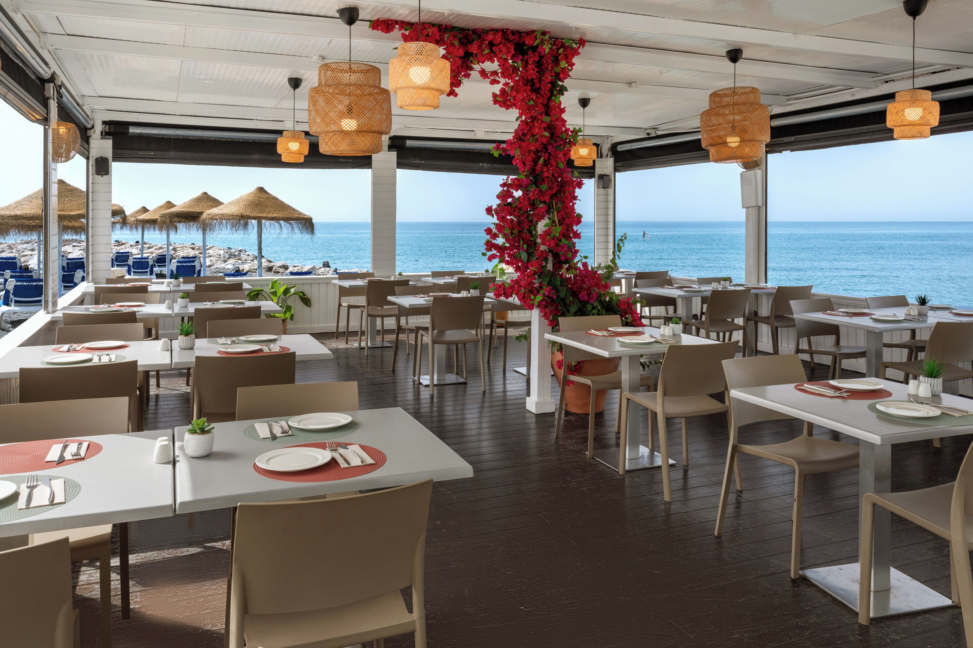 Un restaurant avec des tables et des chaises, une vue sur la mer et des guirlandes lumineuses.