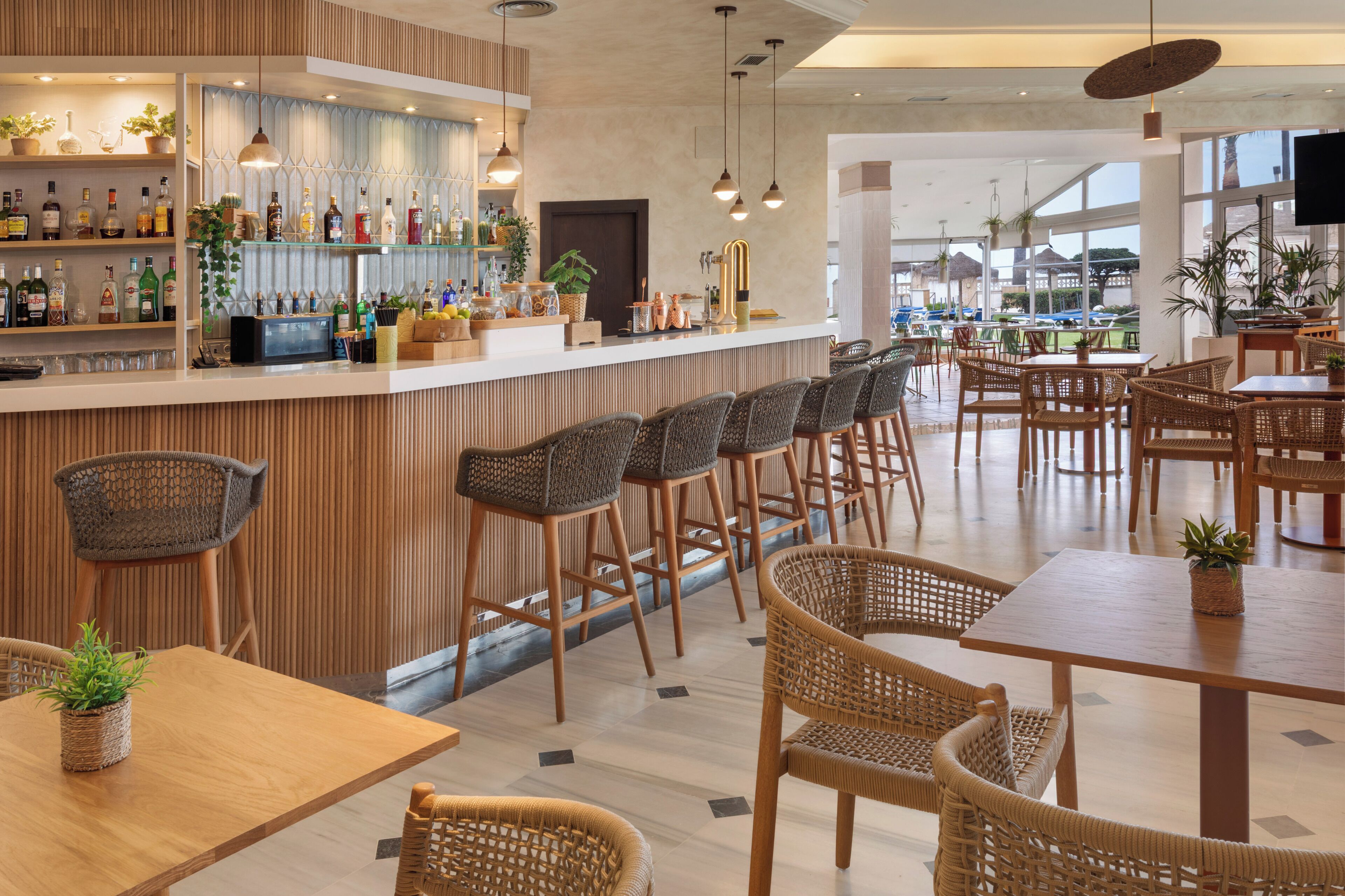 Un bar moderno con una selección de botellas de licor, sillas de mimbre y vistas al exterior.