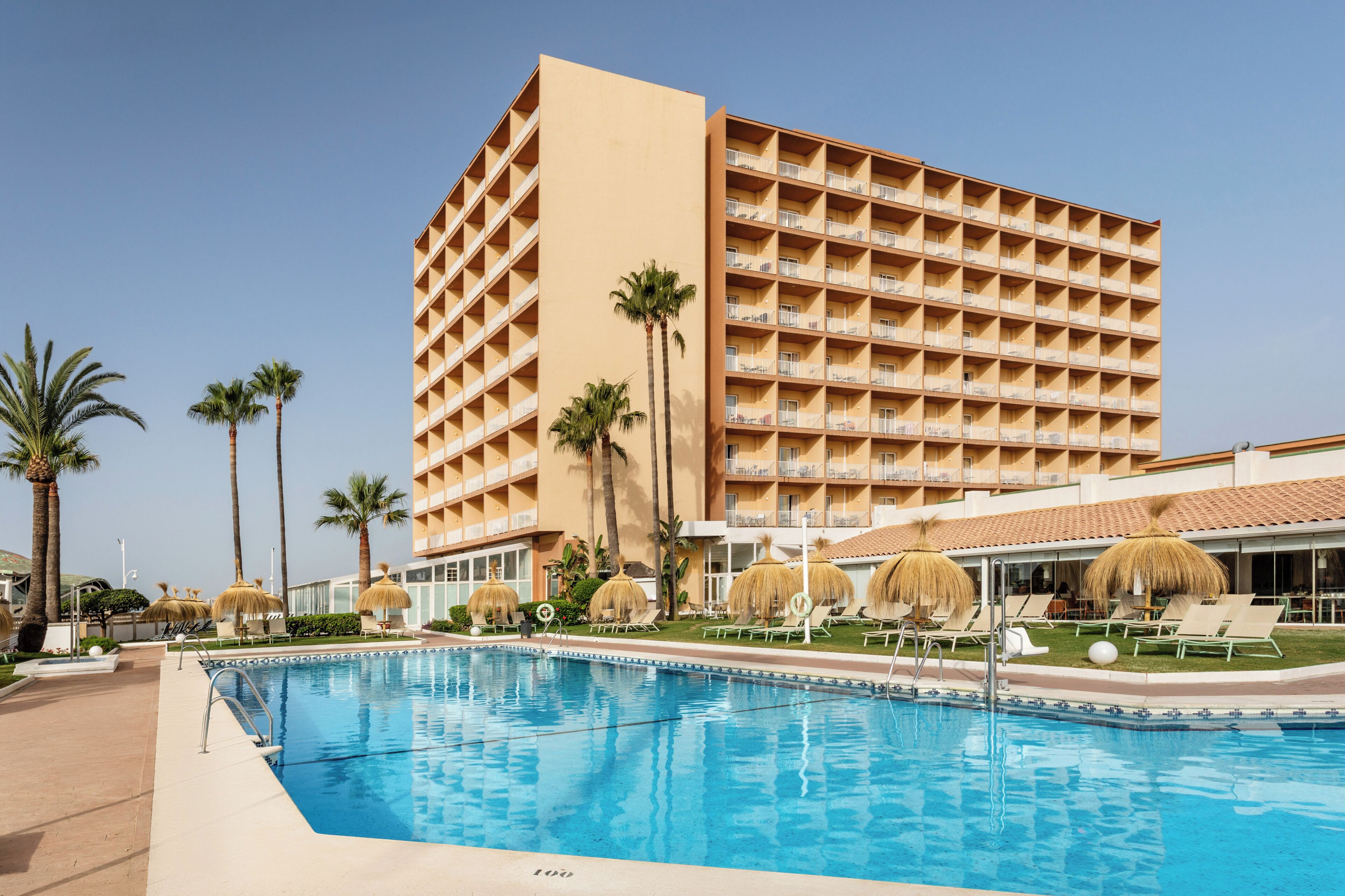Un hôtel doté d’une piscine, de palmiers et d’un bâtiment agrémenté de nombreux balcons.