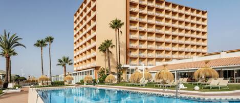 Un hôtel doté d’une piscine, de palmiers et d’un bâtiment agrémenté de nombreux balcons.