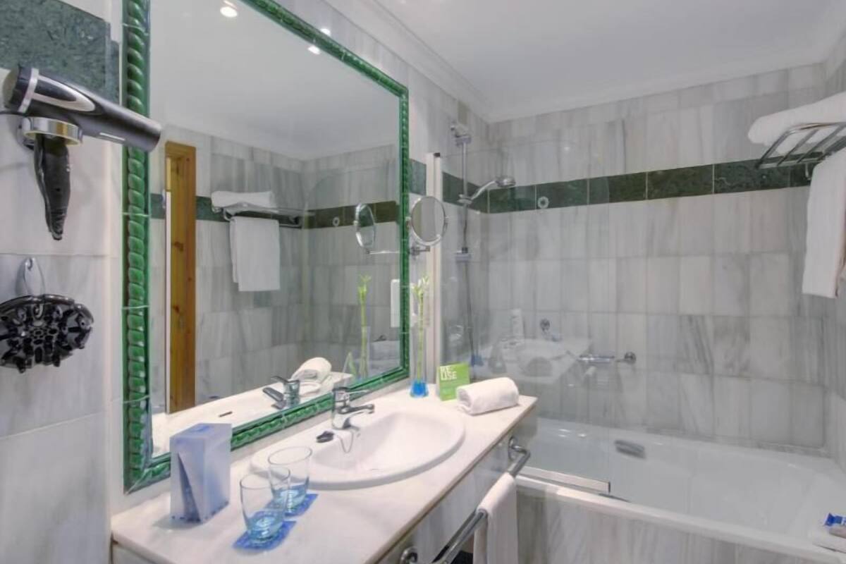 A bathroom with a large mirror, two sinks, a bathtub, and a shower.