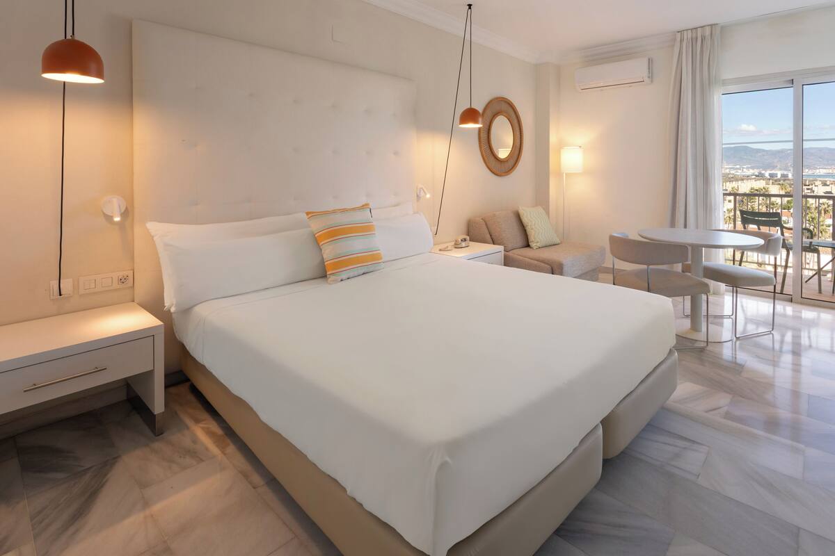 A modern hotel room with a large bed, bedside tables, a desk, and a balcony with a view.