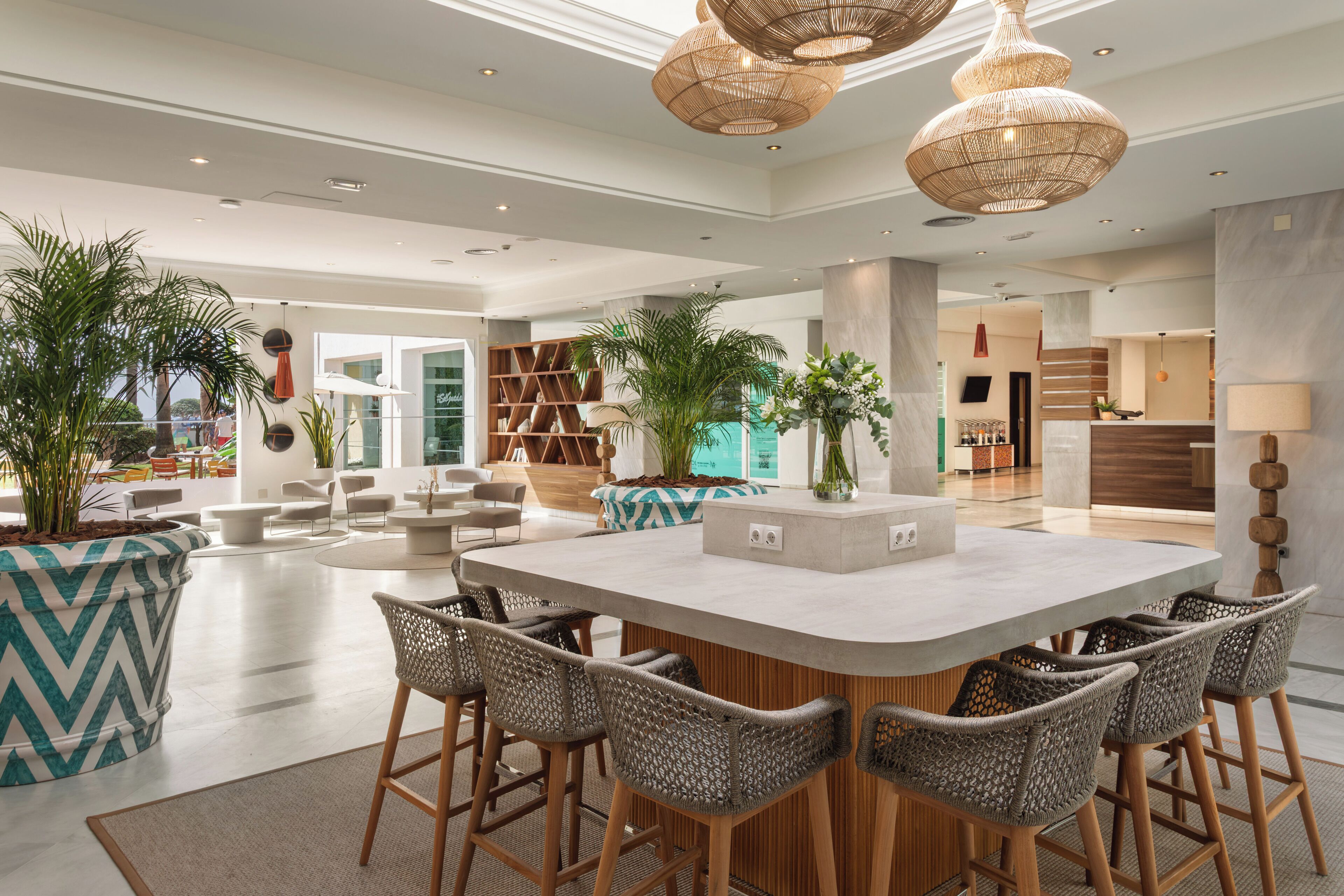 A spacious indoor area with a central island, bar stools, and hanging wicker lamps.
