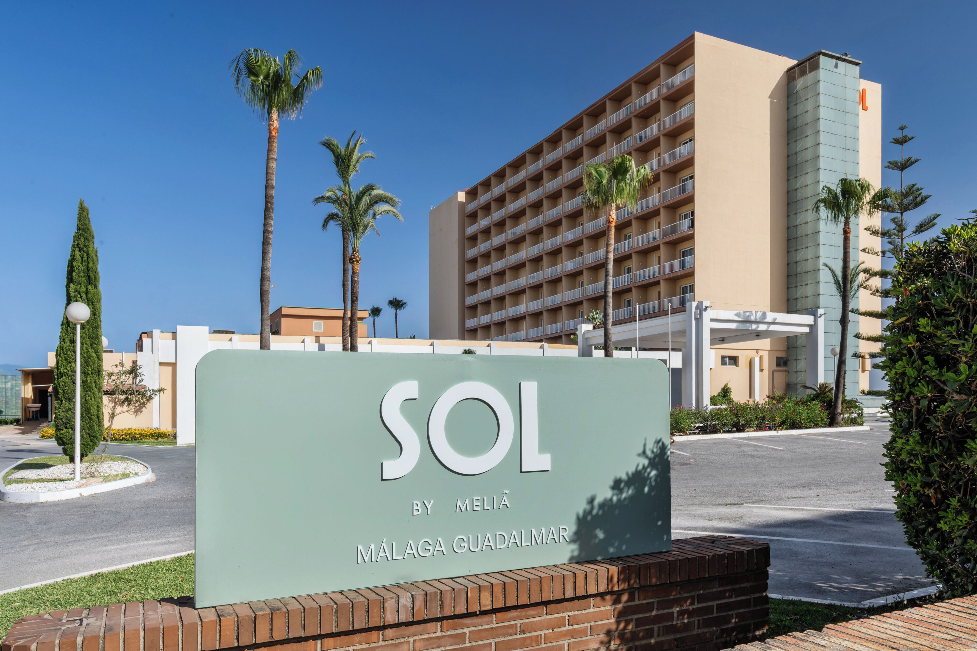 A hotel sign with 'SOL BY MELIA MÁLAGA GUADALMAR' written on it, surrounded by palm trees and a parking lot.