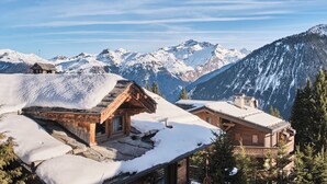 A wooden chalet with a snow-covered roof, surrounded by snow-covered mountains and pine trees. - Lake Hôtel Courchevel 1850 (Courchevel)