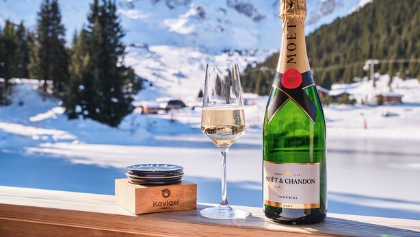 A bottle of Moët & Chandon champagne and a glass on a wooden surface with a snowy mountain backdrop. - Lake Hôtel Courchevel 1850 (Courchevel)