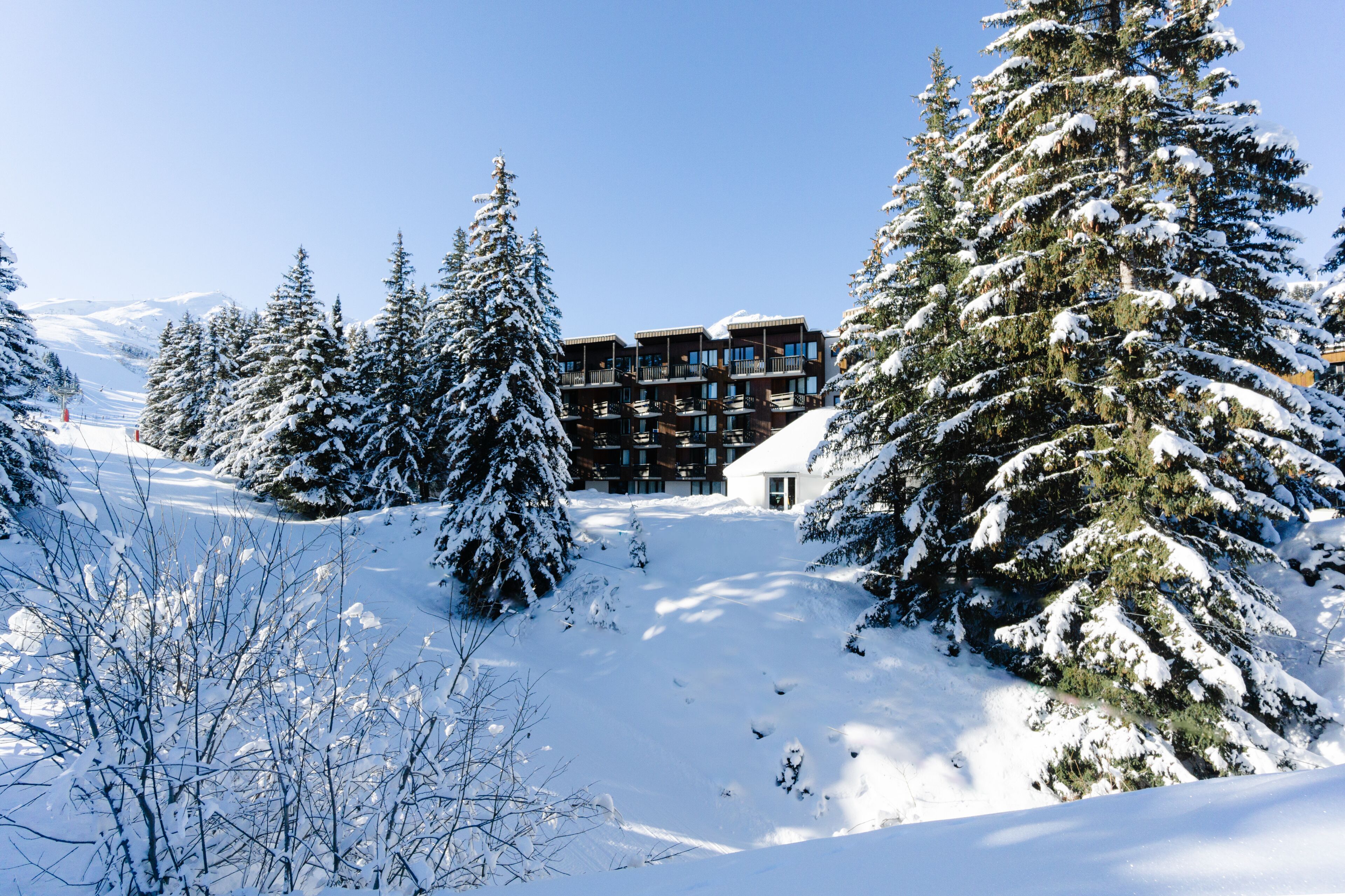 A snow-covered lodge with multiple balconies, surrounded by snow-laden trees and a clear sky.