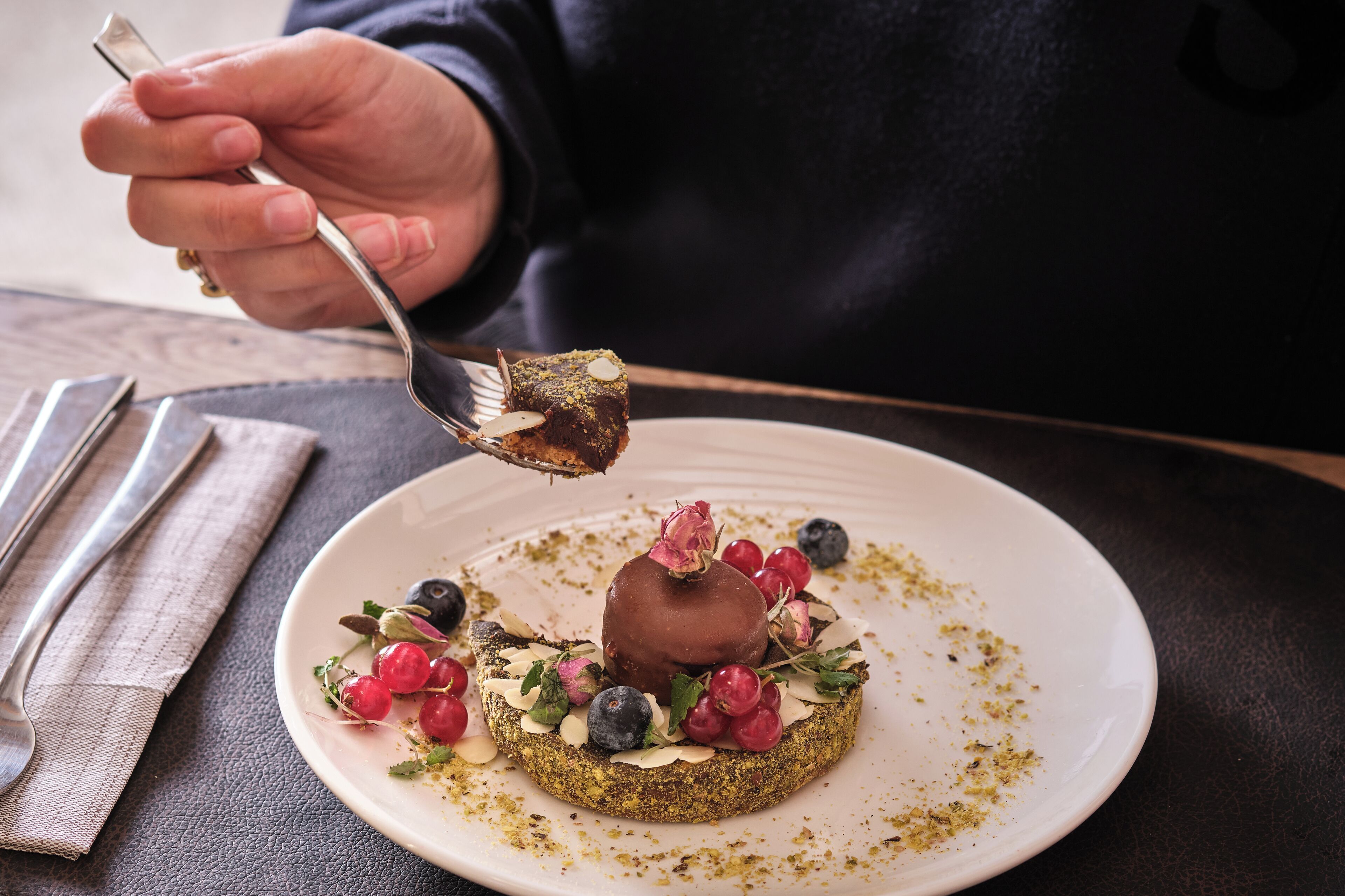 Une personne utilise une fourchette pour manger un dessert dans une assiette contenant des fruits rouges et des noix.