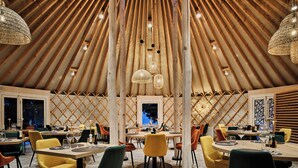 A modern dining area with wooden slats on the ceiling, round tables, and colorful chairs. - Lake Hôtel Courchevel 1850 (Courchevel)