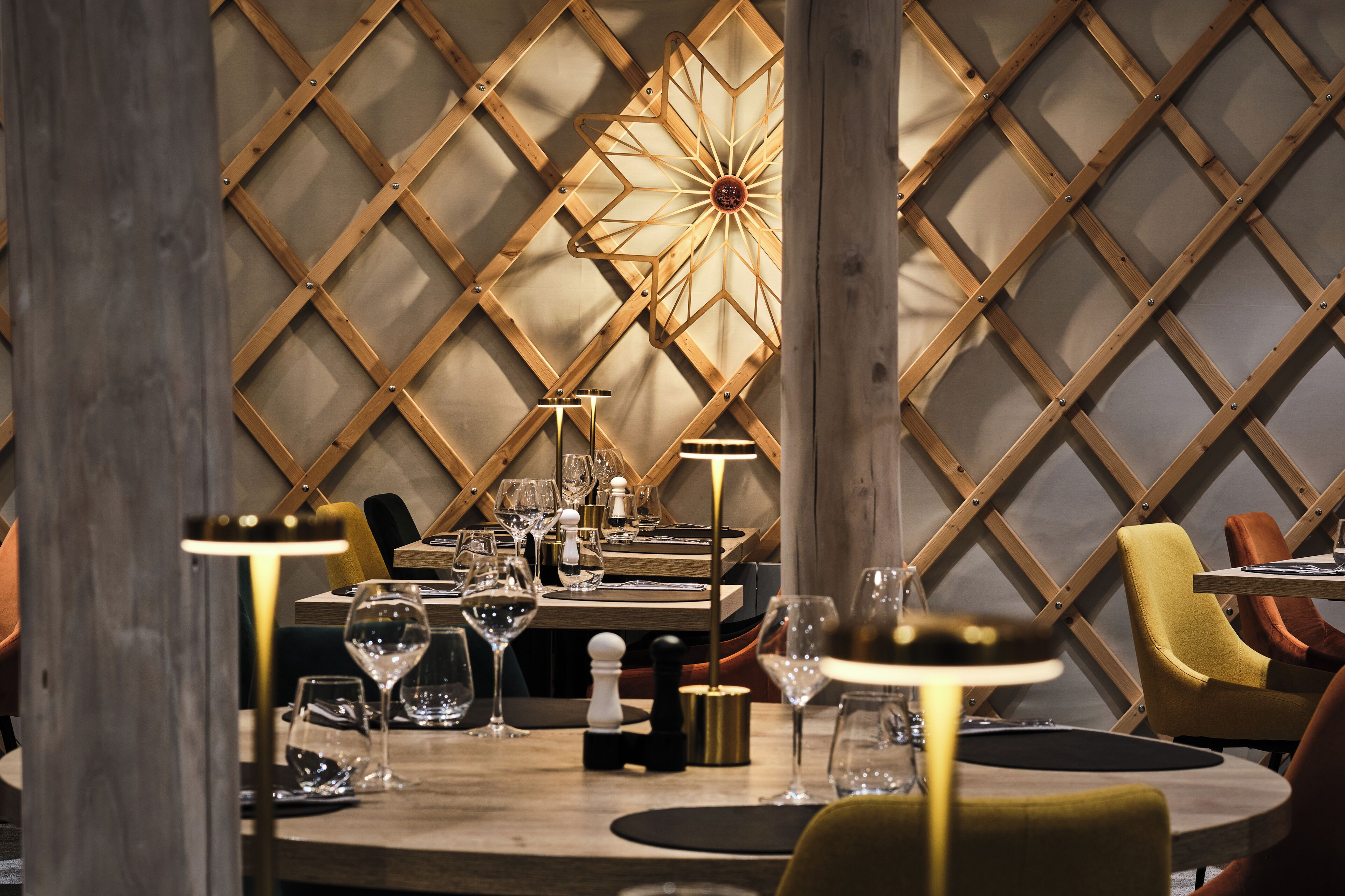 A dining area with a wooden lattice wall, a central chandelier, and modern furnishings.