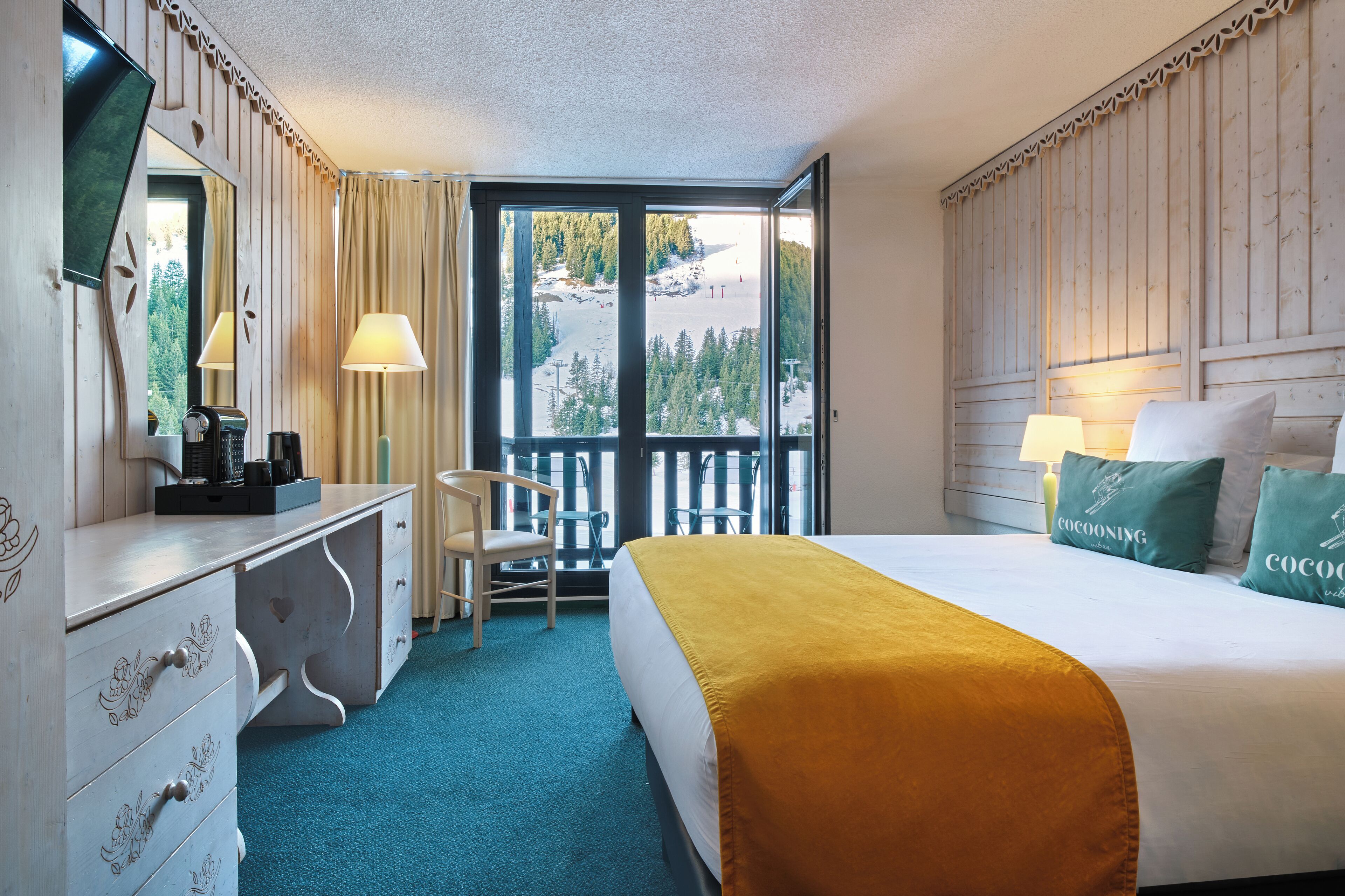 A hotel room with a bed, a desk, a chair, a large window with a view of a snowy landscape, and a balcony.