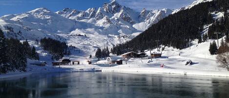 A snow-covered mountain landscape with a lake, buildings, and ski slopes.