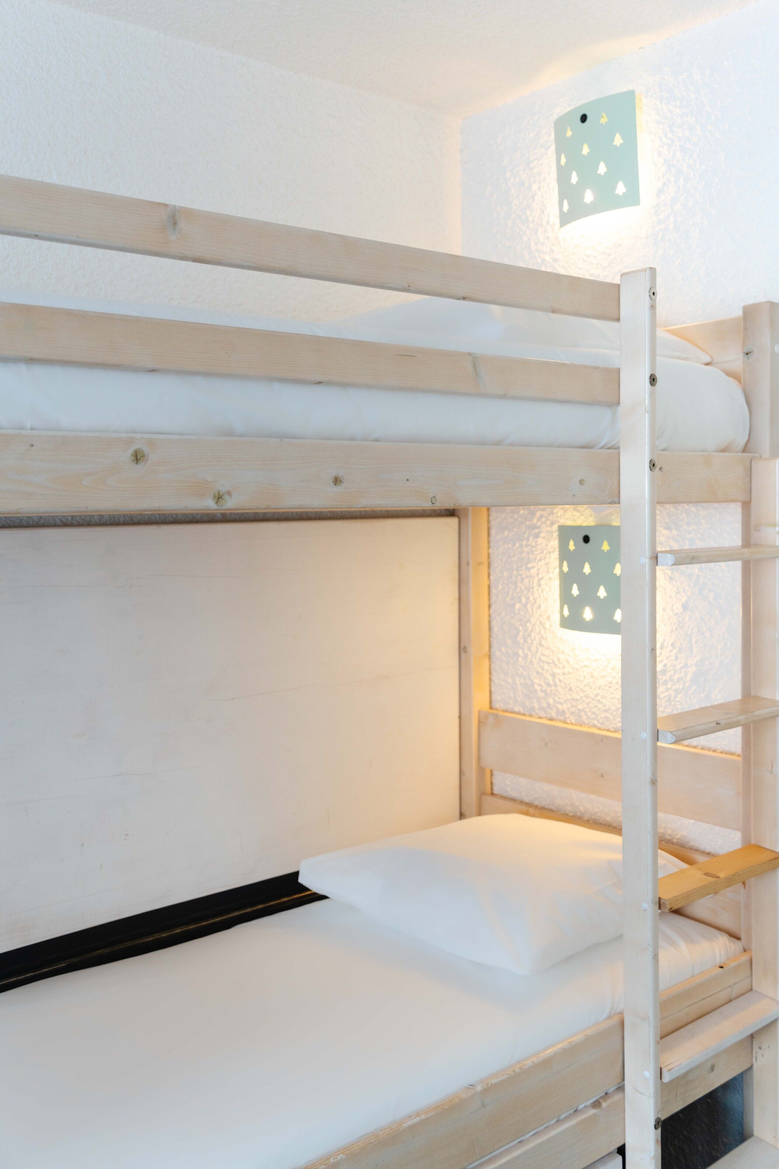 A bunk bed with a ladder, a white mattress, and a wall-mounted light fixture.