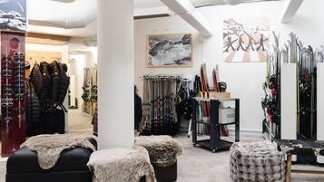 Un magasin d’articles de ski où l’on trouve des rangées de skis, de planches de snowboard et de bâtons de ski. On y trouve également des bancs et un grand pilier au centre.