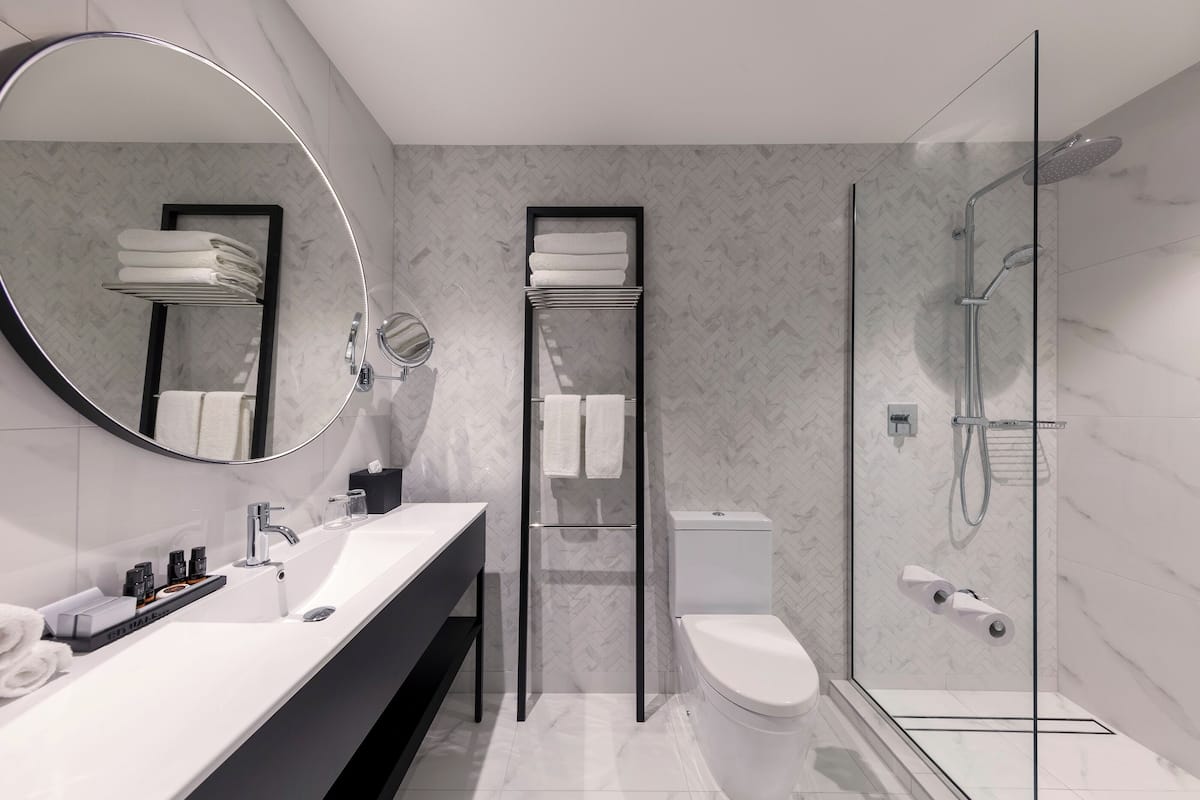 A modern bathroom with a large mirror, a glass-enclosed shower, a toilet, and a sink with a towel rack.