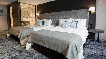A hotel room with two beds, a glass shower enclosure, and a bedside table with a lamp.
