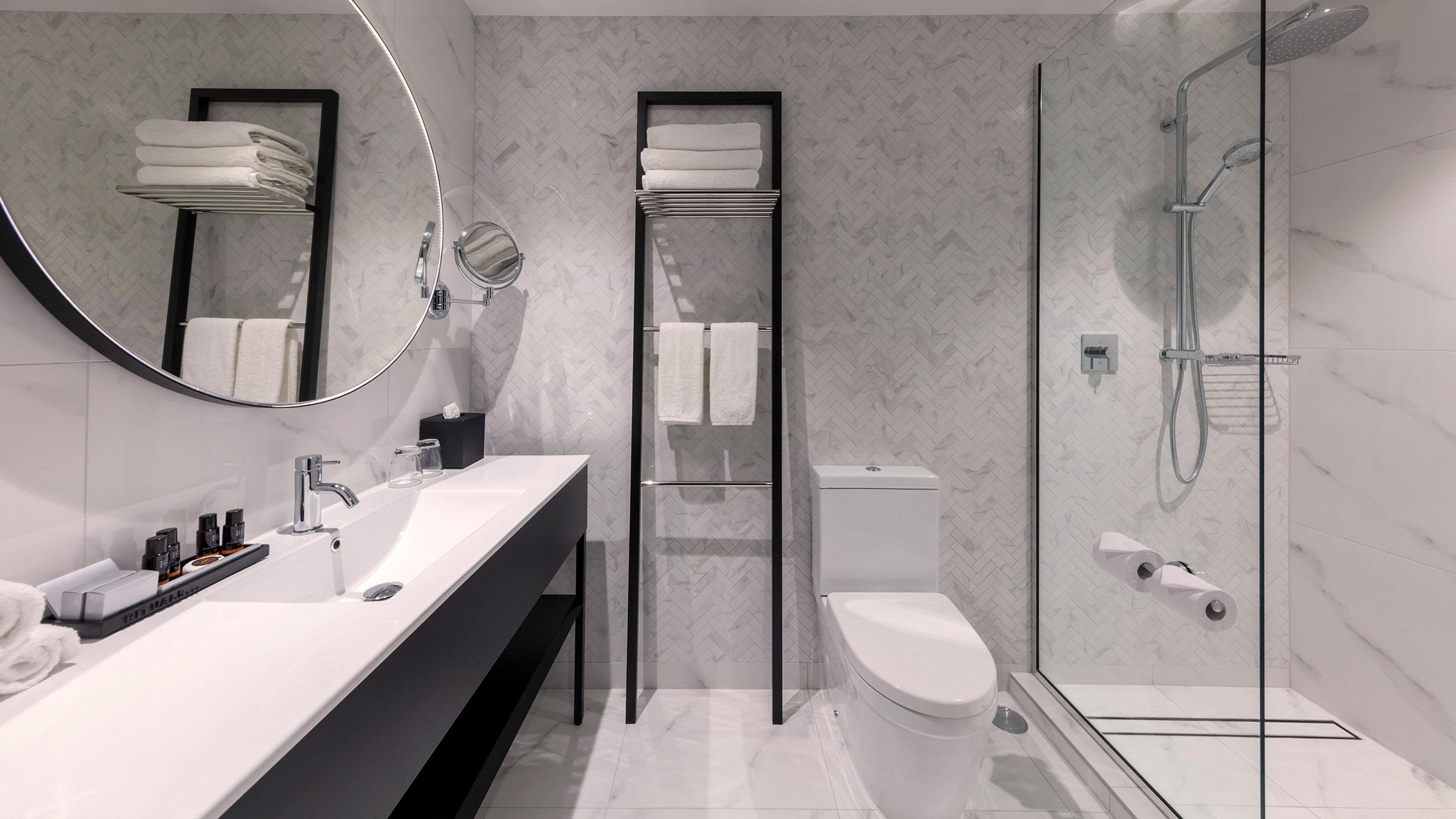 A modern bathroom with a white sink, a toilet, a glass shower enclosure, and a mirror with a towel rack.