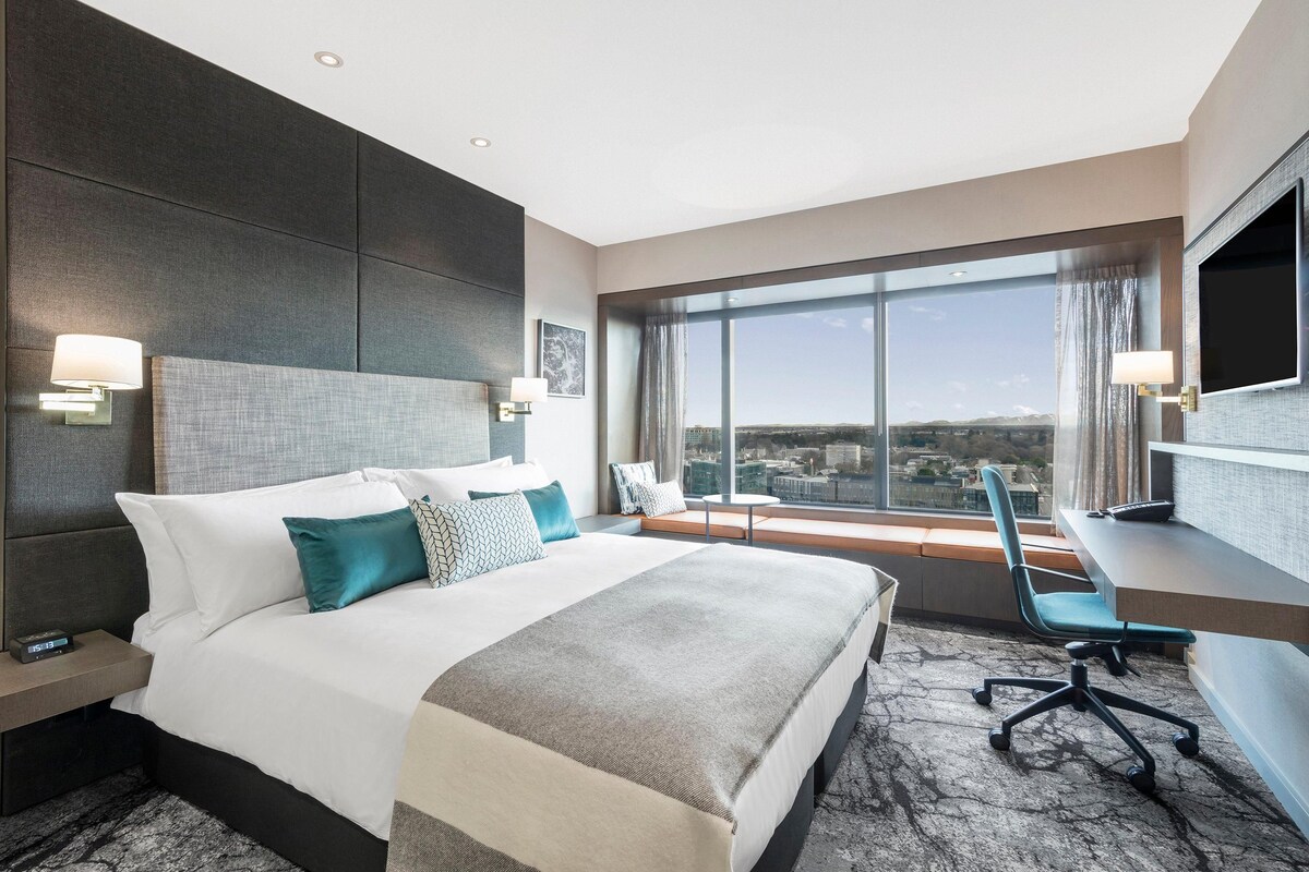 Ein modernes Hotelzimmer mit einem großen Bett, einem Schreibtisch und Blick auf die Stadt.