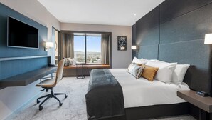 Ett modernt hotellrum med en stor säng, ett skrivbord med en stol, en platt-TV och ett fönster med utsikt över staden.