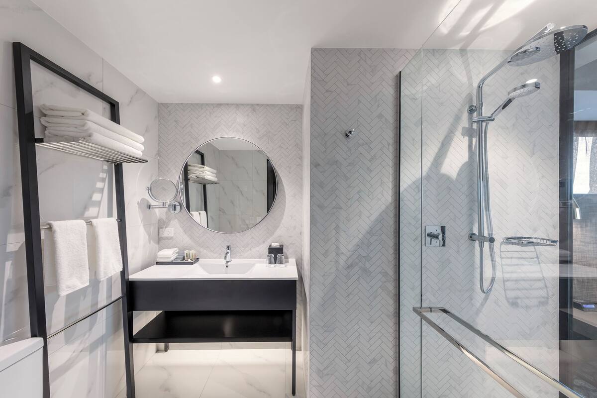 Une salle de bain moderne avec une douche à parois de verre, un miroir rond et un meuble-lavabo noir.