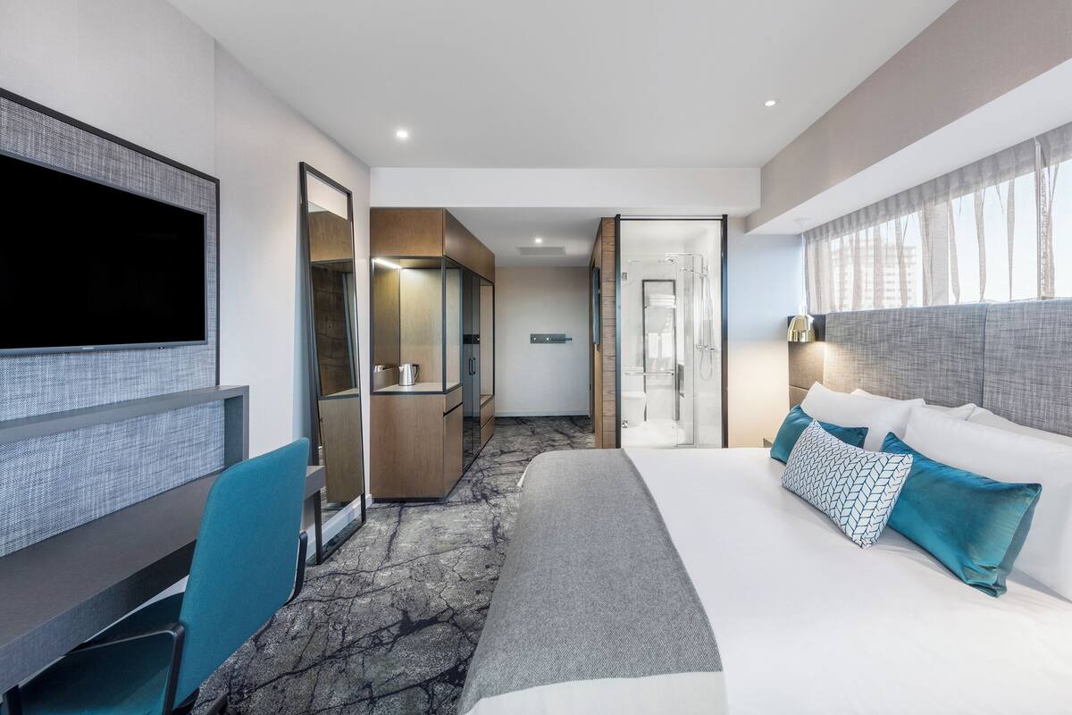 Une chambre d’hôtel comprenant un lit, un bureau avec une chaise, une télévision, une salle de bain et un espace douche.