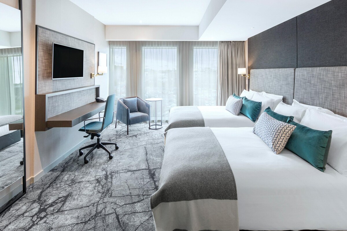 Ein Hotelzimmer mit einem großen Bett, einem Schreibtisch, einem Sessel und einem Fernseher.