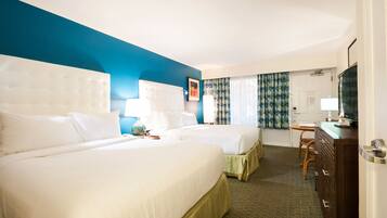 A hotel room with two beds, a television, a desk, and a window with curtains.