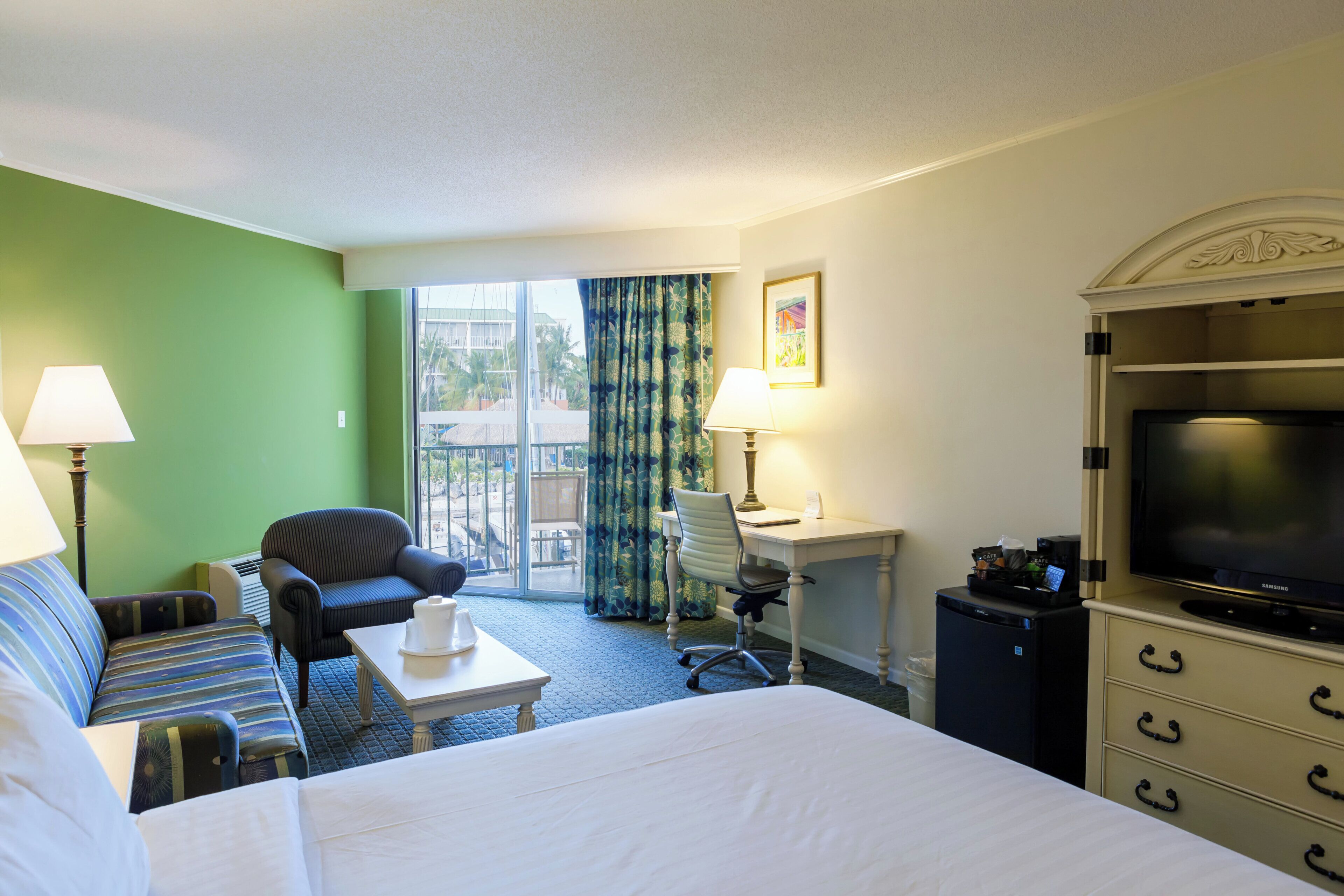 A hotel room with a bed, a desk, a chair, a television, and a small refrigerator.