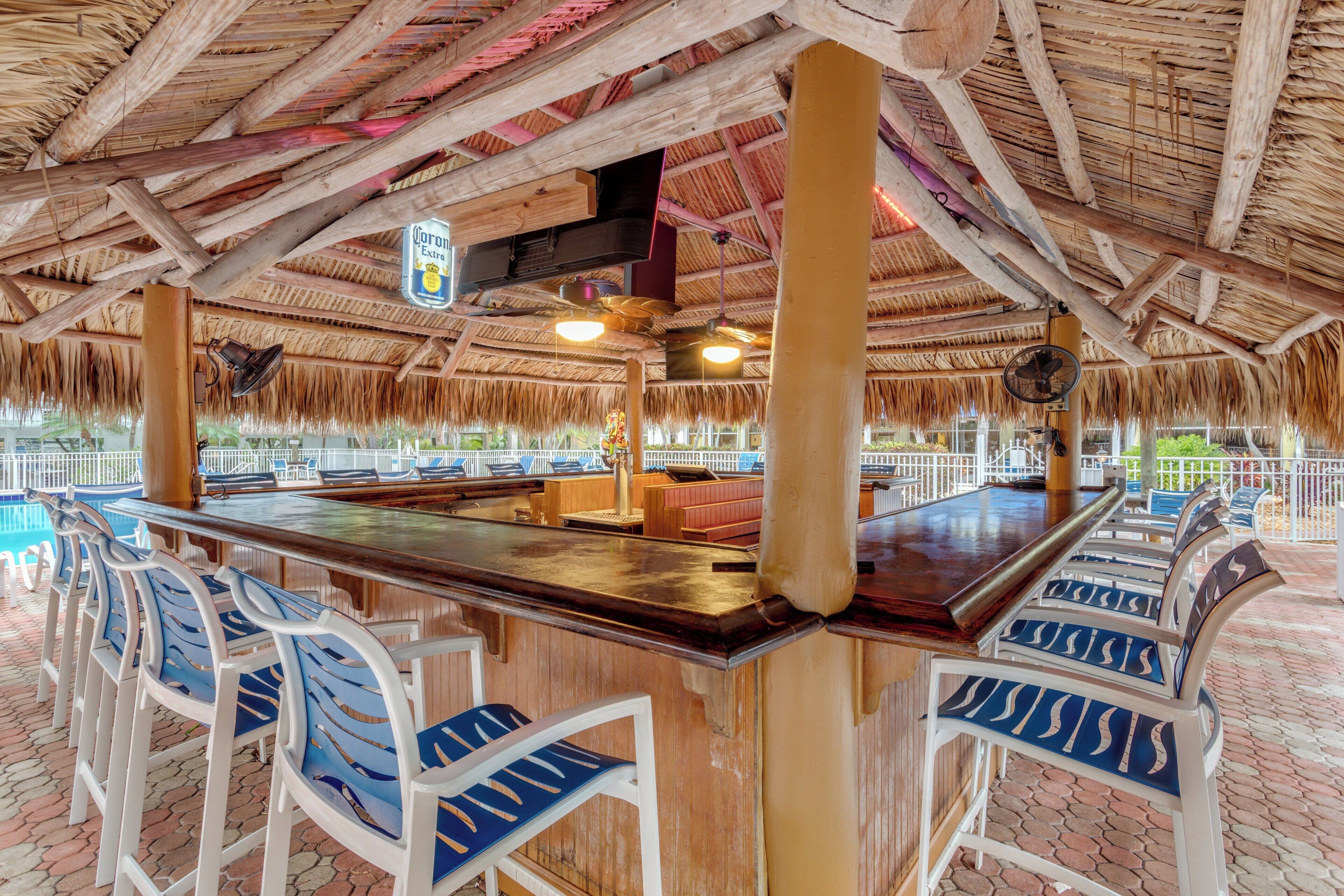 Zona de bar con techo de paja, vigas de madera y vista a la piscina.