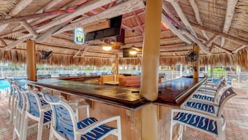 A bar area with a thatched roof, wooden beams, and a poolside view.