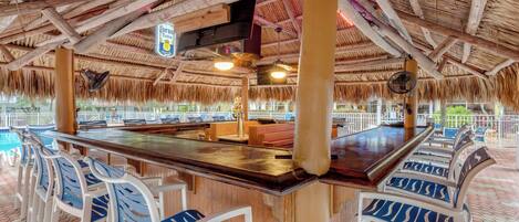 A bar area with a thatched roof, wooden beams, and a poolside view.