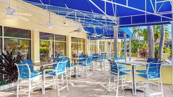 Un espace extérieur aménagé en terrasse, avec des tables et des chaises, de grandes fenêtres et une structure de tonnelle bleue.