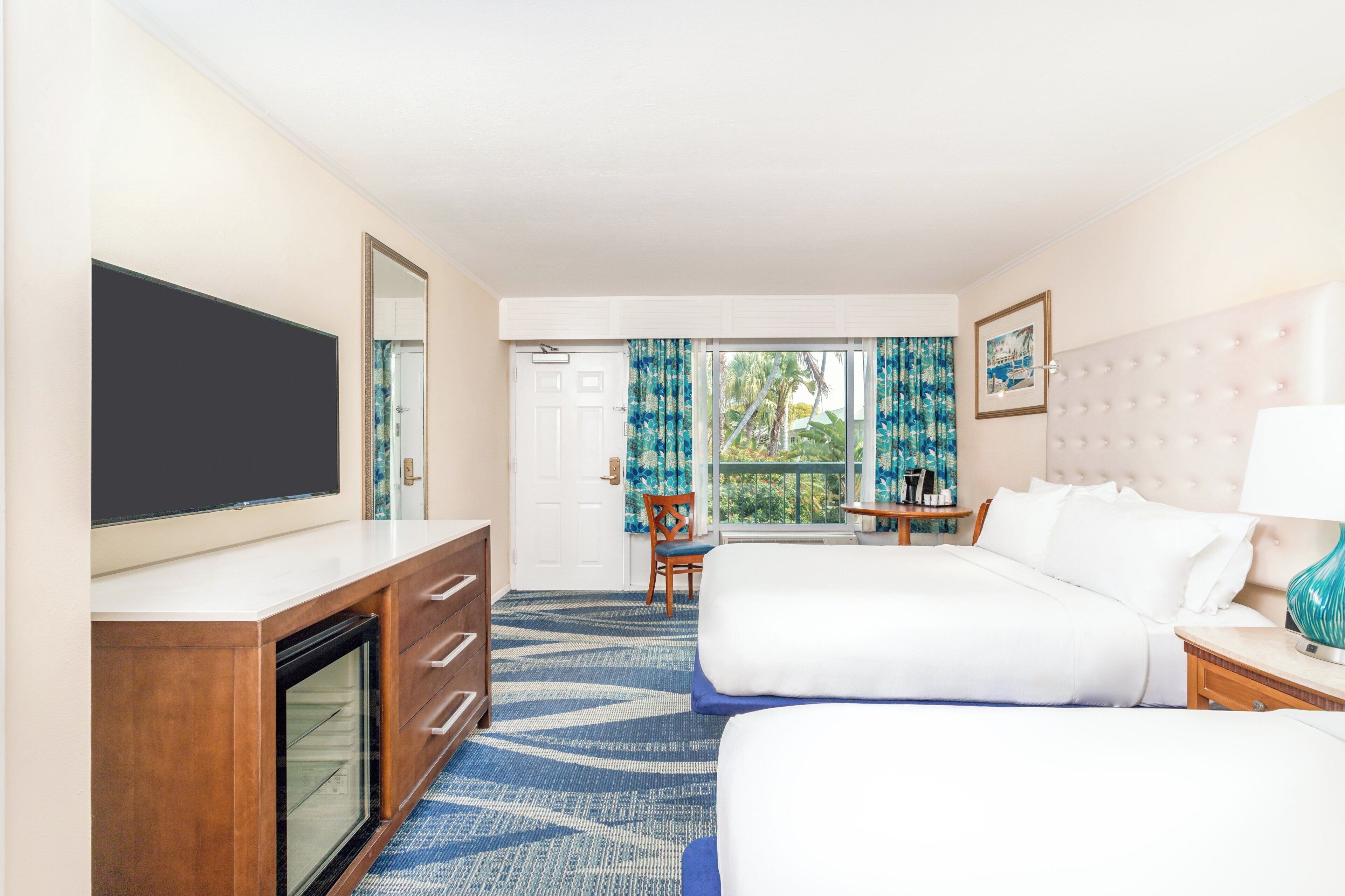 A hotel room with two beds, a TV, a desk, and a window with curtains.