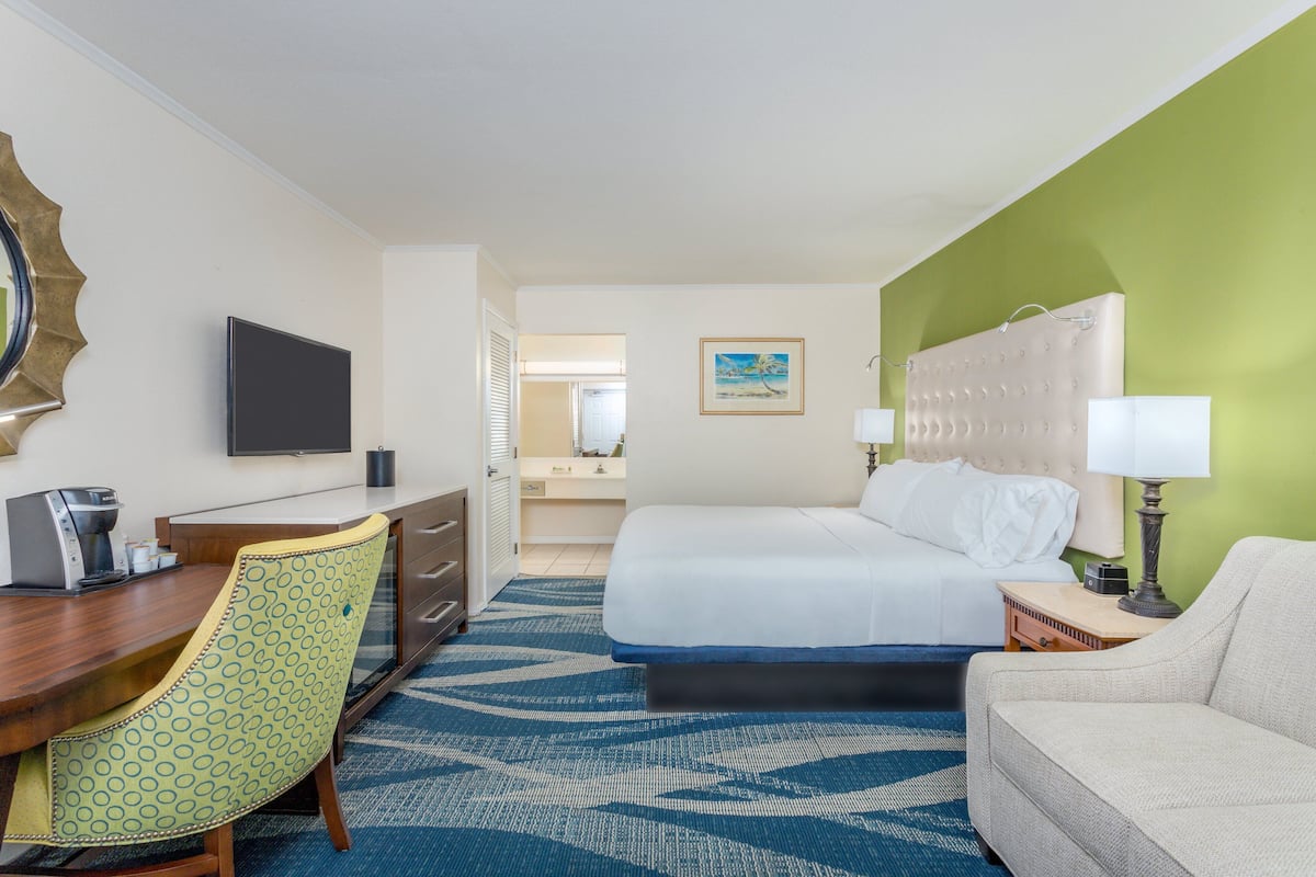 A hotel room with a bed, a desk with a chair, a television, a lamp, and a painting on the wall.