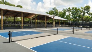 A tennis court with a covered seating area and trees in the background.