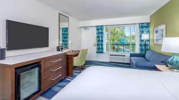 A hotel room with a large bed, a desk with a chair, a television, and a window with curtains.