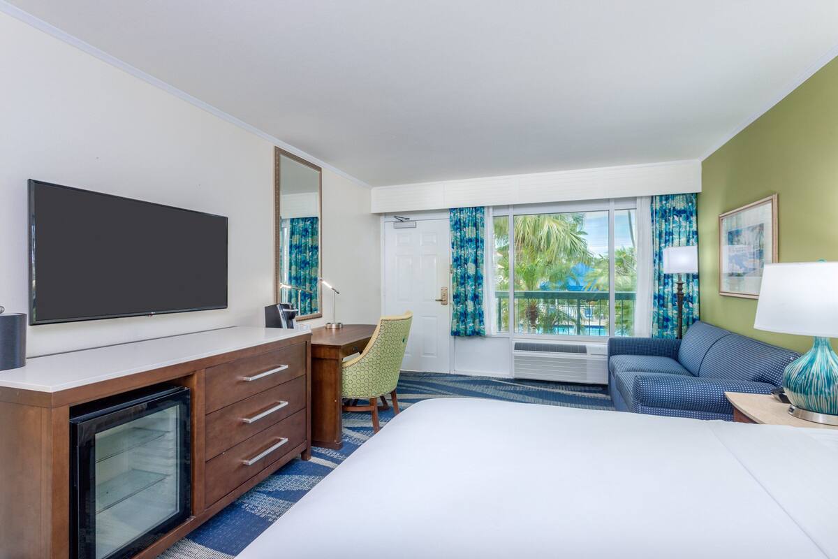 Una habitación de hotel con una cama grande, un escritorio con silla, televisión y ventana con cortinas.