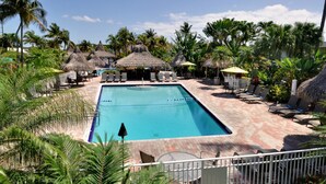 A rectangular swimming pool with a tiled deck, surrounded by lounge chairs and thatched umbrellas.