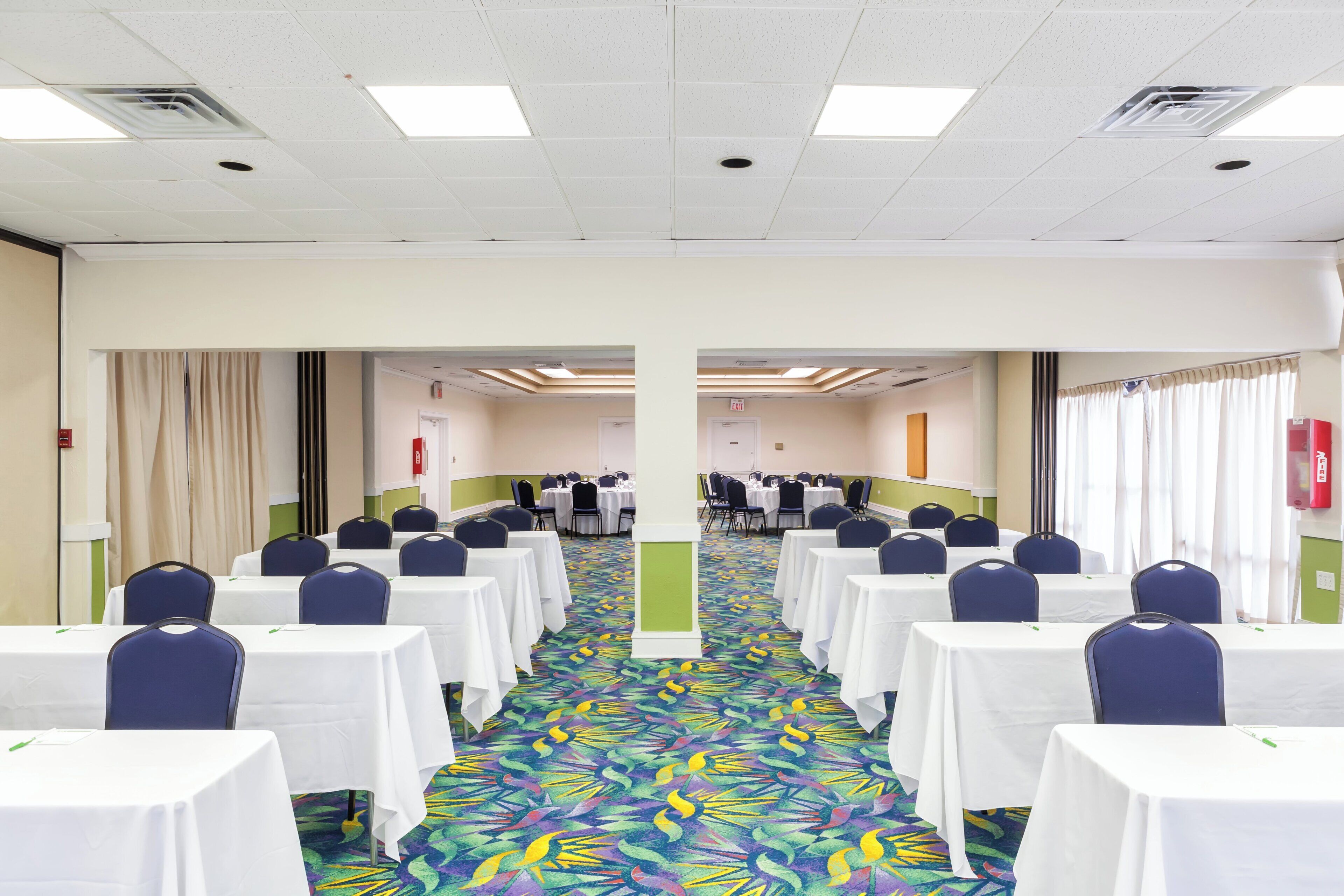 A conference room with tables and chairs, a patterned carpet, and a ceiling with recessed lighting.