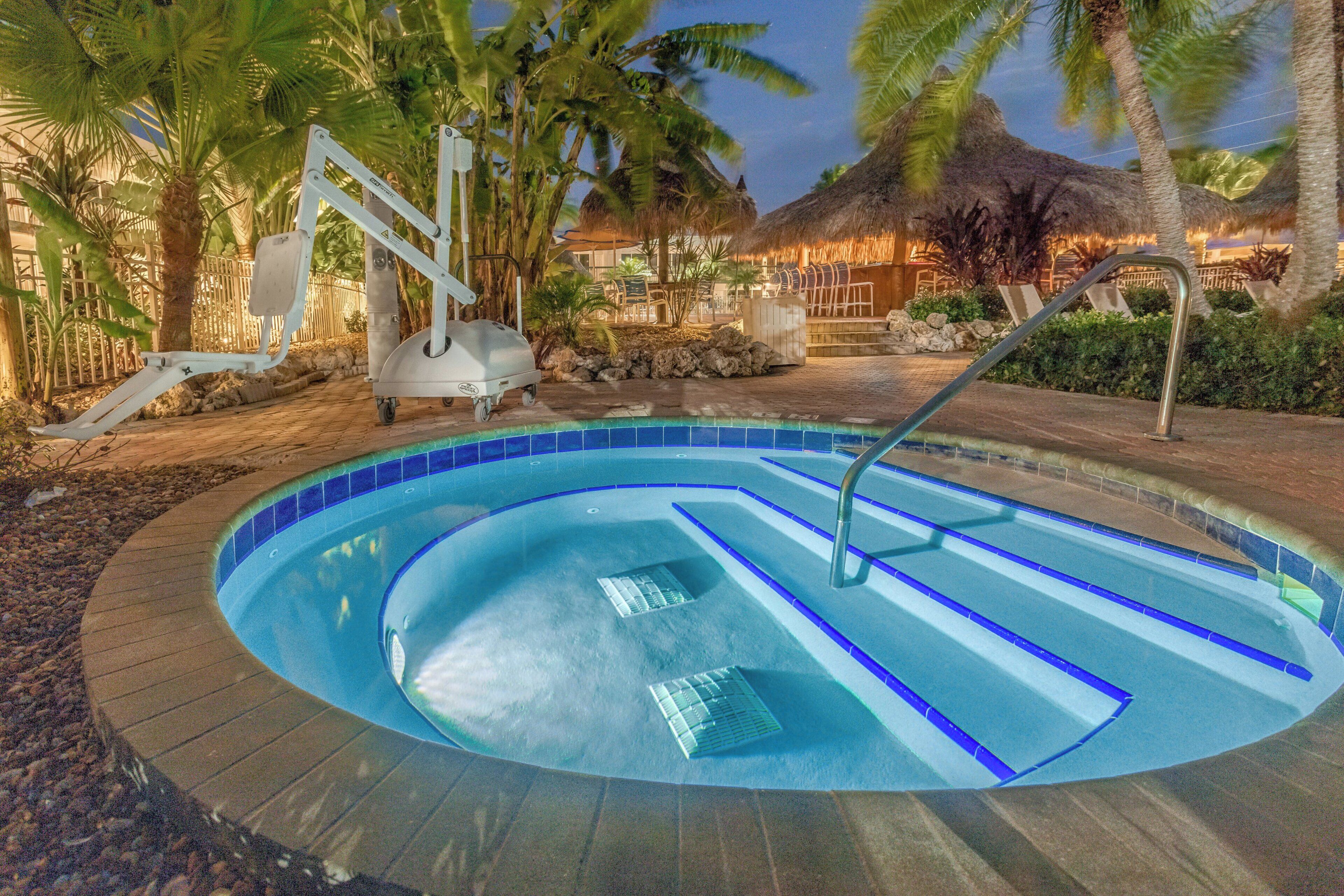 Una piscina con borde curvo, rodeada de palmeras y una estructura con techo de paja.