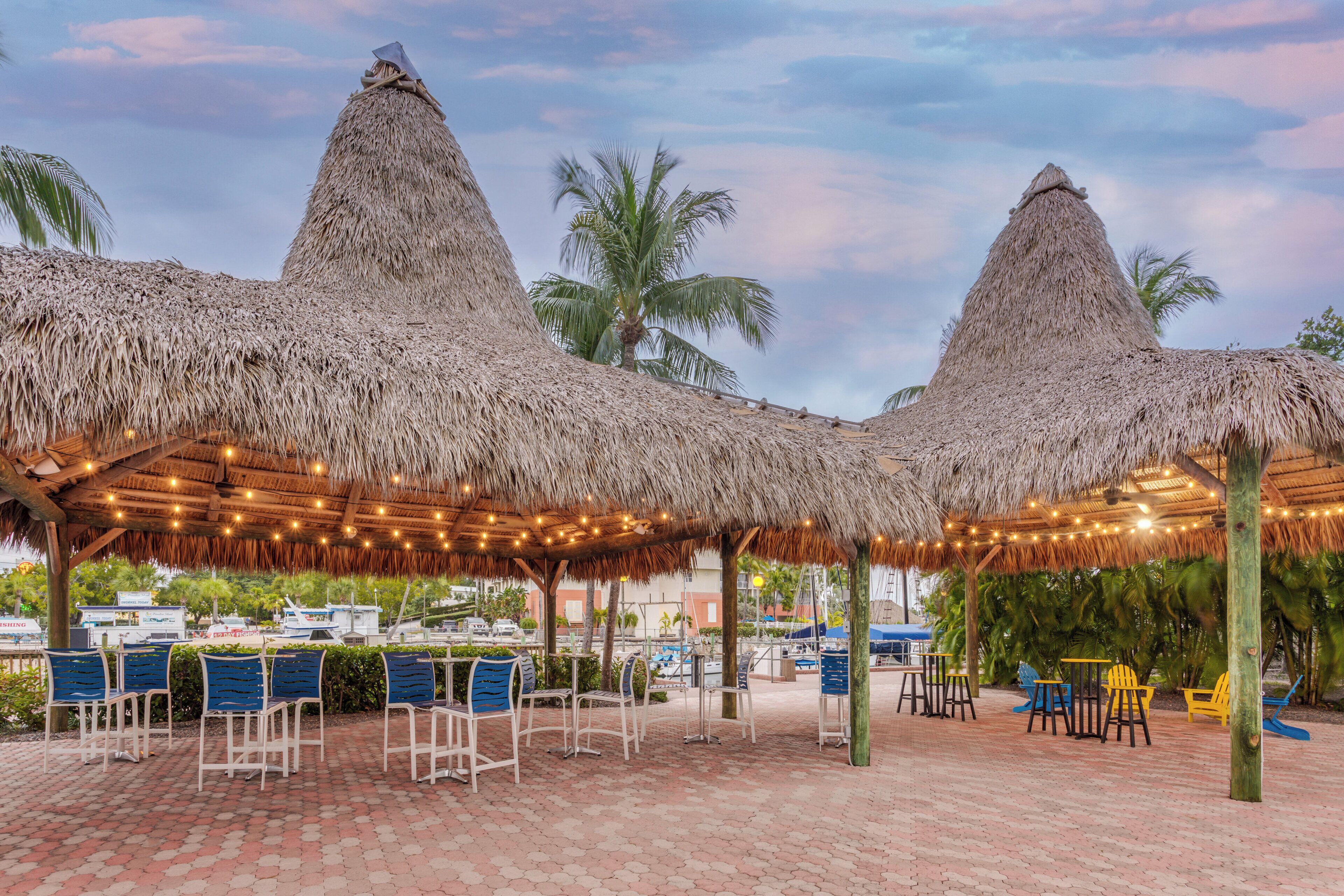 A covered outdoor seating area with thatched roofs, chairs, and string lights.