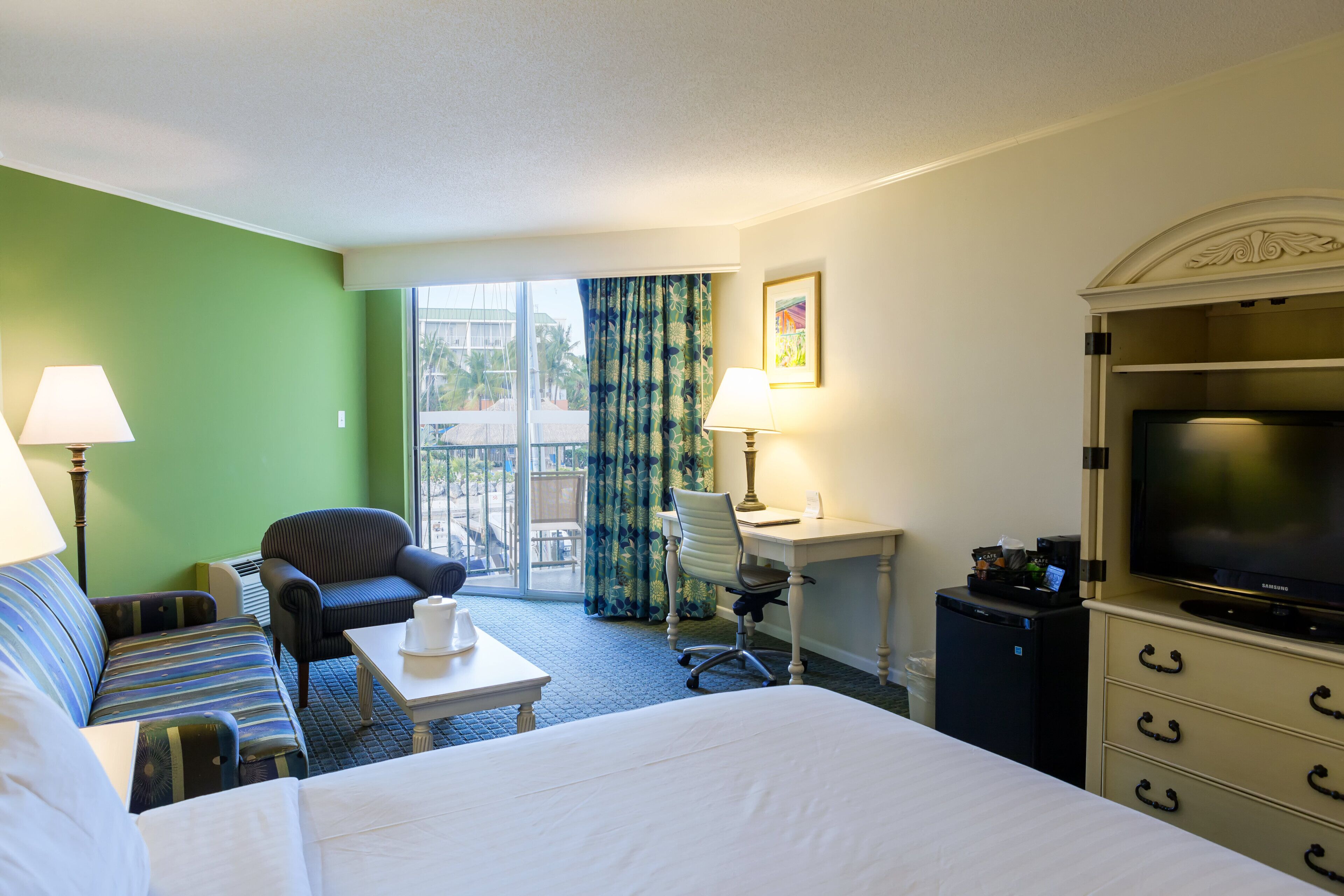 Een hotelkamer met een bed, een bureau, een stoel, een televisie en een kleine koelkast.