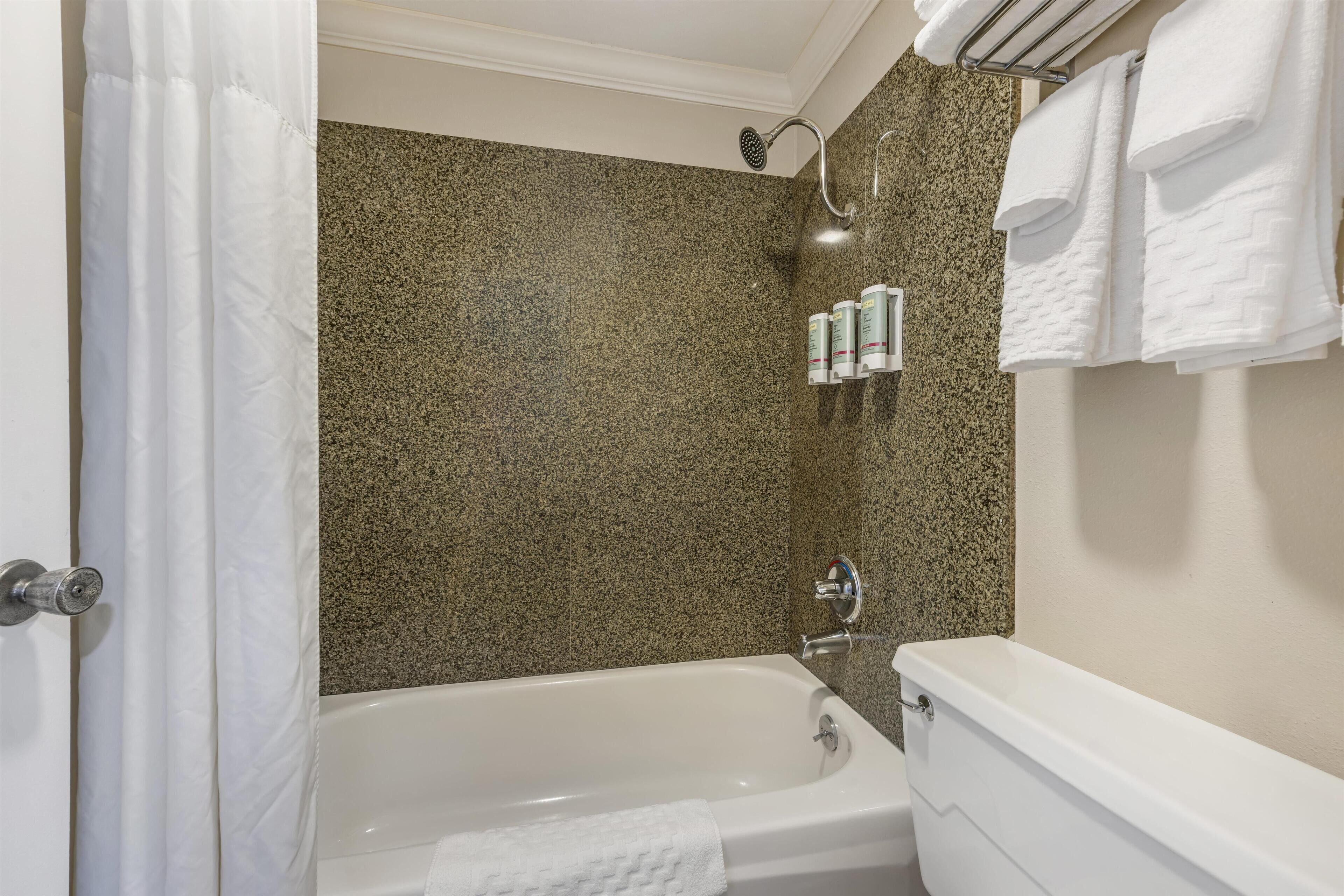 A bathroom with a granite wall, a bathtub, a showerhead, and a towel rack with towels.