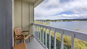 Een balkon met twee houten stoelen, uitzicht op een meer en een verre oever met gebouwen en heuvels.