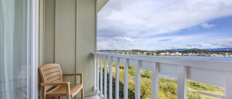 A balcony with two wooden chairs and a table, overlooking a scenic view of a body of water and distant landscape.