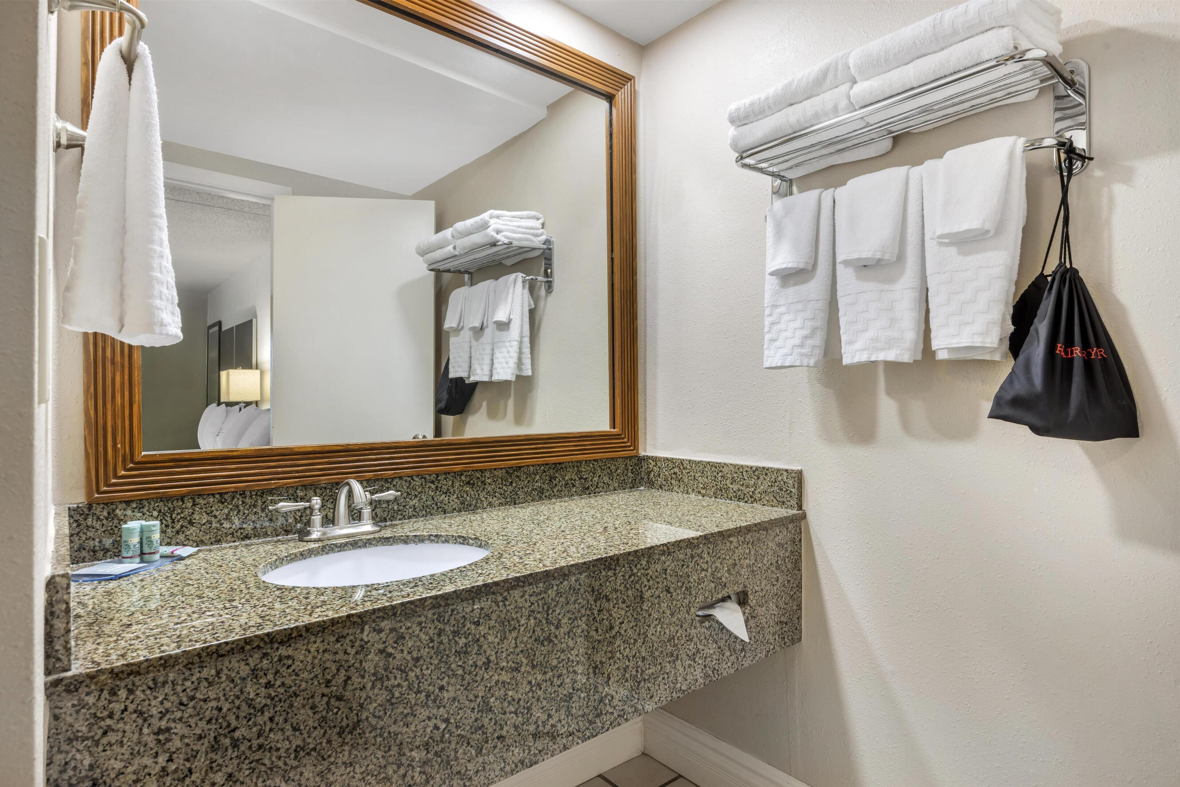A bathroom with a granite countertop sink, a mirror with a wooden frame, and towels neatly arranged on a rack.