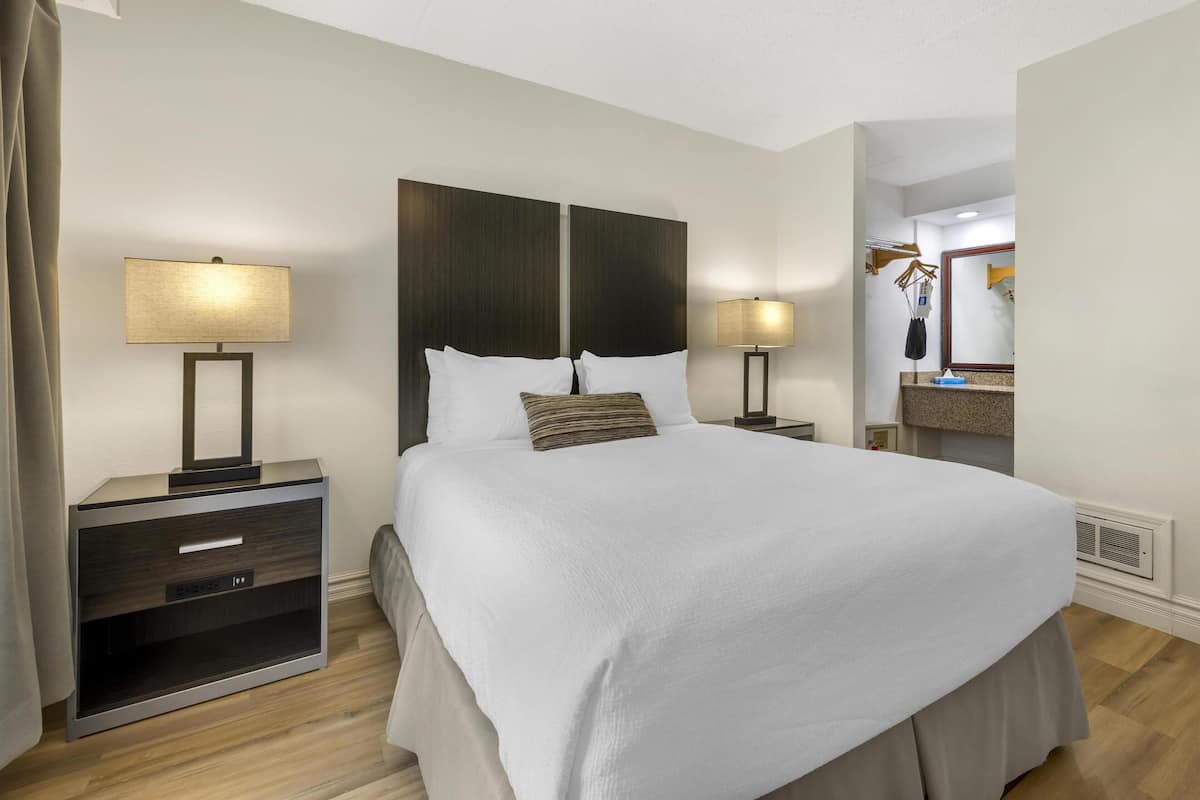 Habitación de hotel con una cama grande, dos mesitas de noche con lámparas, un aparador con cajones y un espejo sobre el aparador.