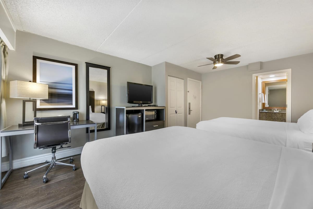 A hotel room with a bed, desk, chair, television, and a ceiling fan.